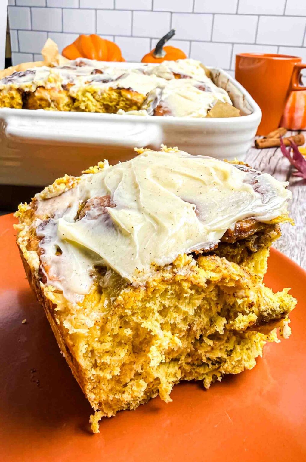 1 cream cheese frosted pumpkin cinnamon roll on a orange plate.