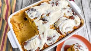 Pumpkin Cinnamon Rolls in pan with 2 already missing. Also glazed with cream cheese frosting