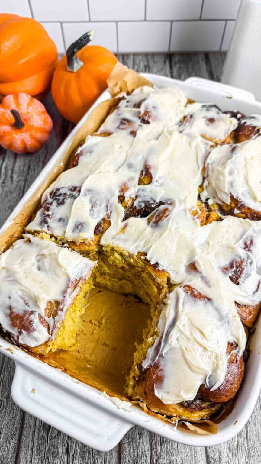baking pan full of pumpkin cinnamon rolls and one missing.