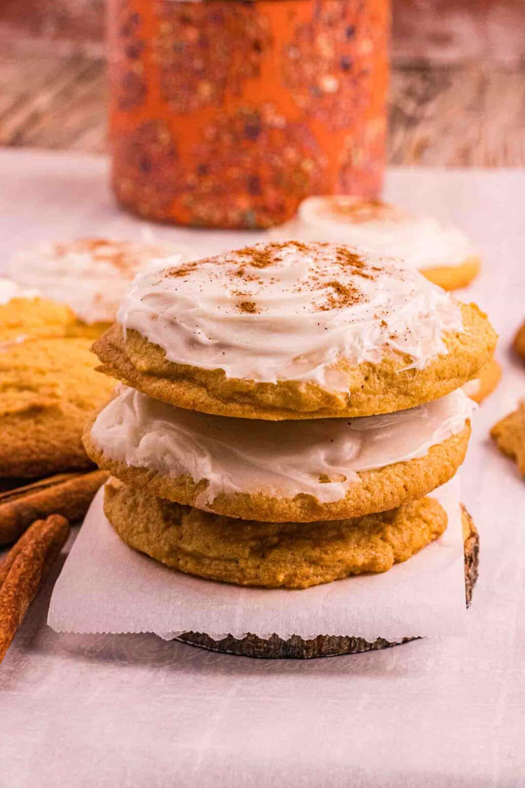 3 pumpkin cookies stack on top of each other surrounded by other frosted cookies