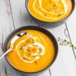 Butternut Squash soup in 2 black bowls topped with some cream and pumpkin seeds