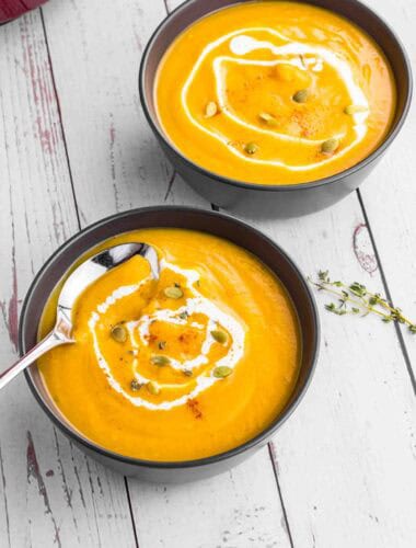 Butternut Squash soup in 2 black bowls topped with some cream and pumpkin seeds