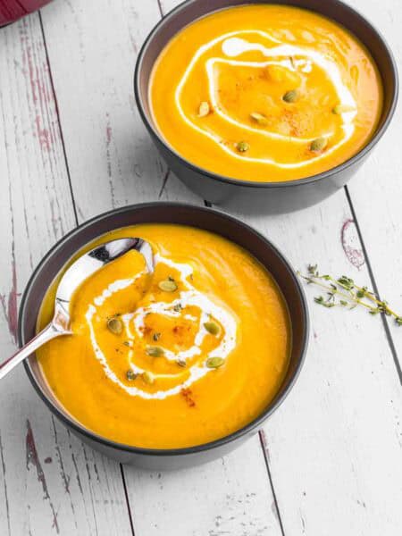 Butternut Squash soup in 2 black bowls topped with some cream and pumpkin seeds