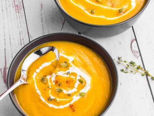 Butternut Squash soup in 2 black bowls topped with some cream and pumpkin seeds