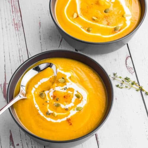 Butternut Squash soup in 2 black bowls topped with some cream and pumpkin seeds