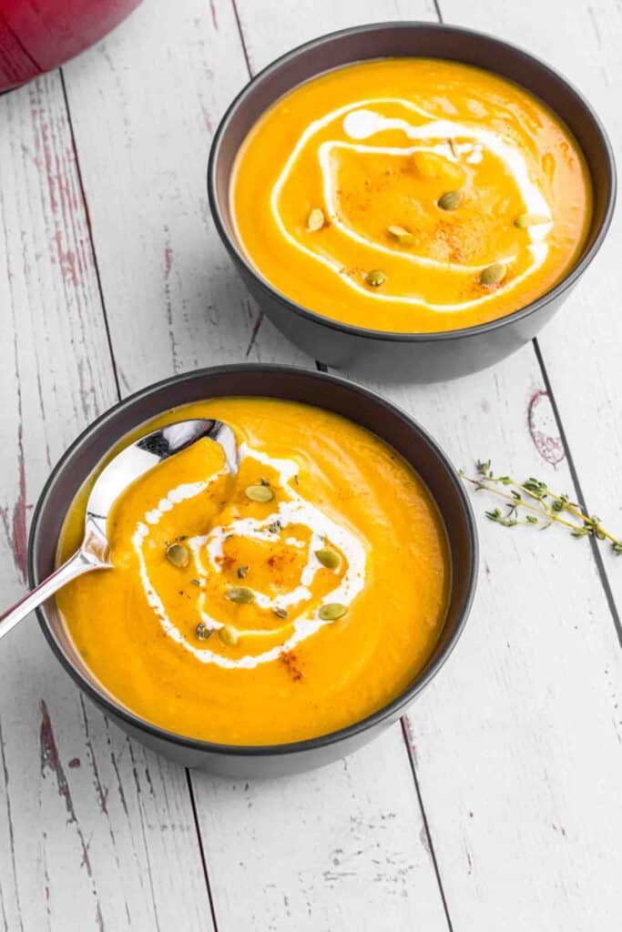 Butternut Squash soup in 2 black bowls topped with some cream and pumpkin seeds