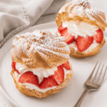 2 German windbeutel or cream puffs with strawberries and whipped cream on a plate