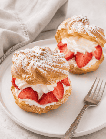 2 German windbeutel or cream puffs with strawberries and whipped cream on a plate