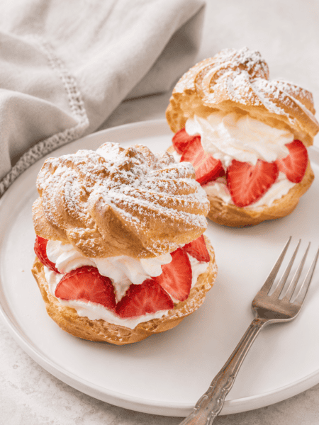 2 German windbeutel or cream puffs with strawberries and whipped cream on a plate