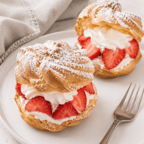 2 German windbeutel or cream puffs with strawberries and whipped cream on a plate