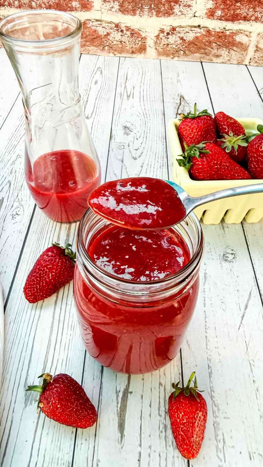 glass of strawberry sauce with a spoonful of it over glass top