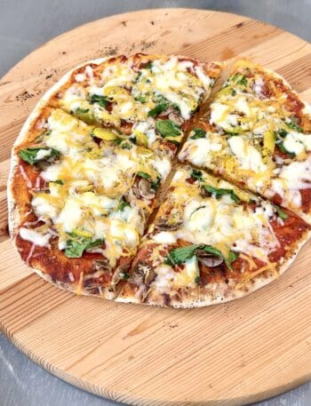 grilled pizza on a round wooden board cut in 4 pieces