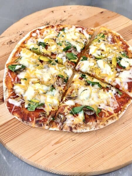 grilled pizza on a round wooden board cut in 4 pieces