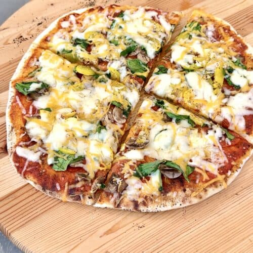 grilled pizza on a round wooden board cut in 4 pieces