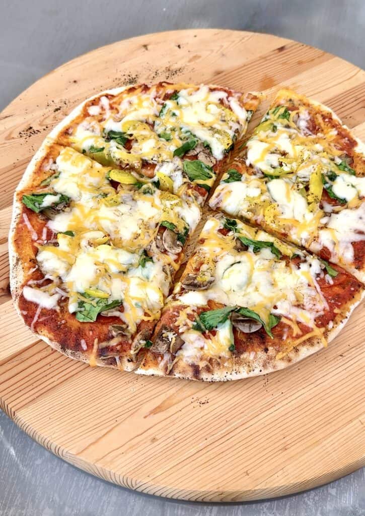 grilled pizza on a round wooden board cut in 4 pieces