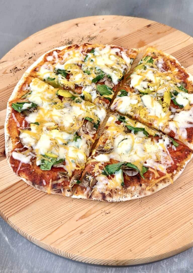 grilled pizza on a round wooden board cut in 4 pieces