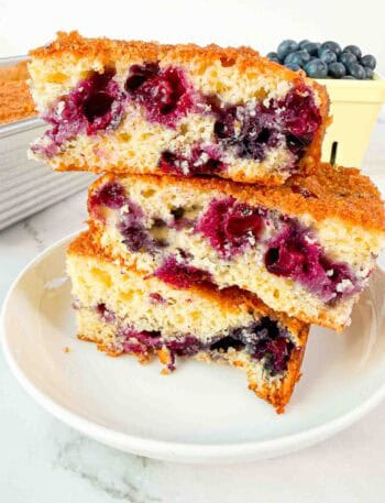 Stacked up blueberry cake squares on a white plate. 3 cake squares high
