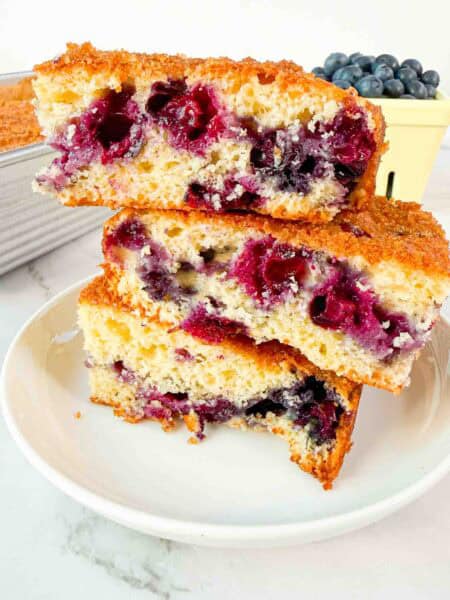 Stacked up blueberry cake squares on a white plate. 3 cake squares high