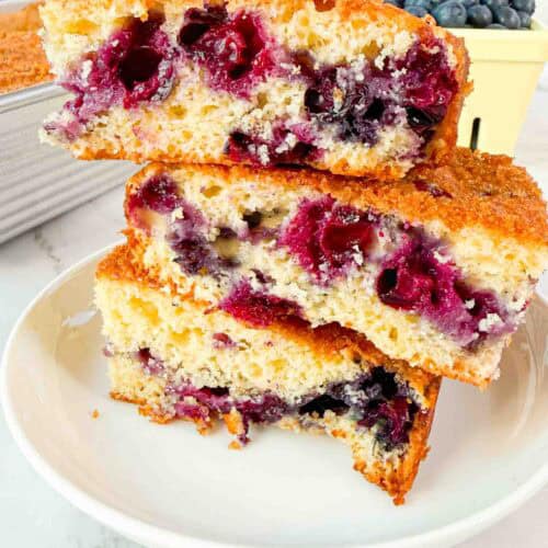 Stacked up blueberry cake squares on a white plate. 3 cake squares high