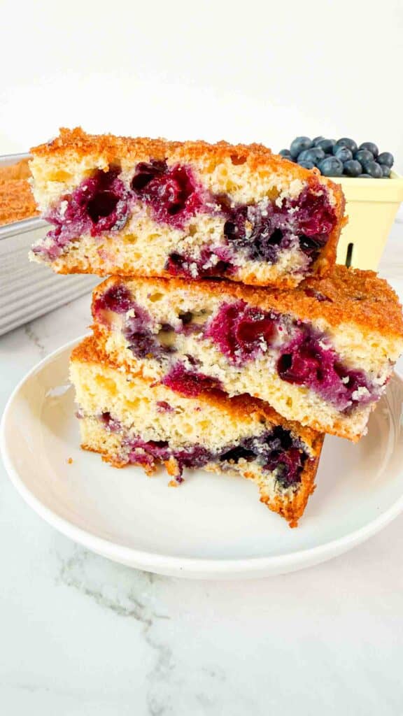 Stacked up blueberry cake squares on a white plate. 3 cake squares high