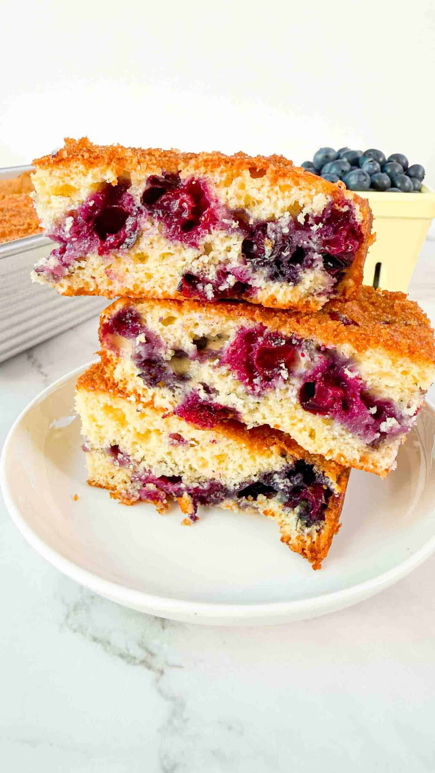 Stacked up blueberry cake squares on a white plate. 3 cake squares high