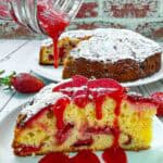 Strawberry Cake slice on white plate being drizzled with strawberry sauce on top