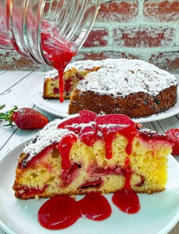 Strawberry Cake slice on white plate being drizzled with strawberry sauce on top