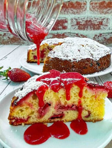 Strawberry Cake slice on white plate being drizzled with strawberry sauce on top