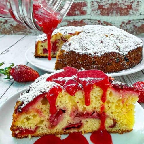 Strawberry Cake slice on white plate being drizzled with strawberry sauce on top