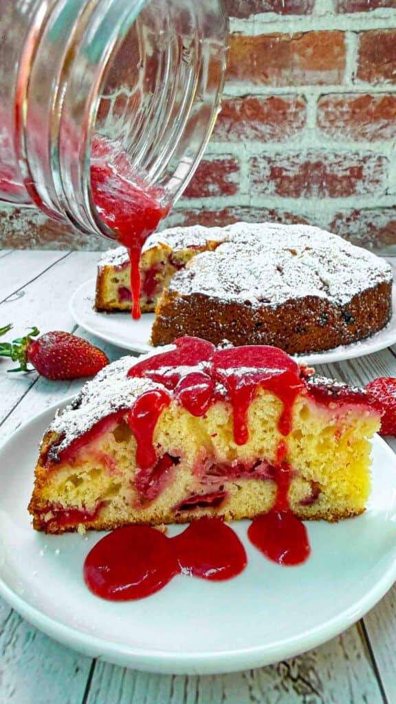 Strawberry Cake slice on white plate being drizzled with strawberry sauce on top