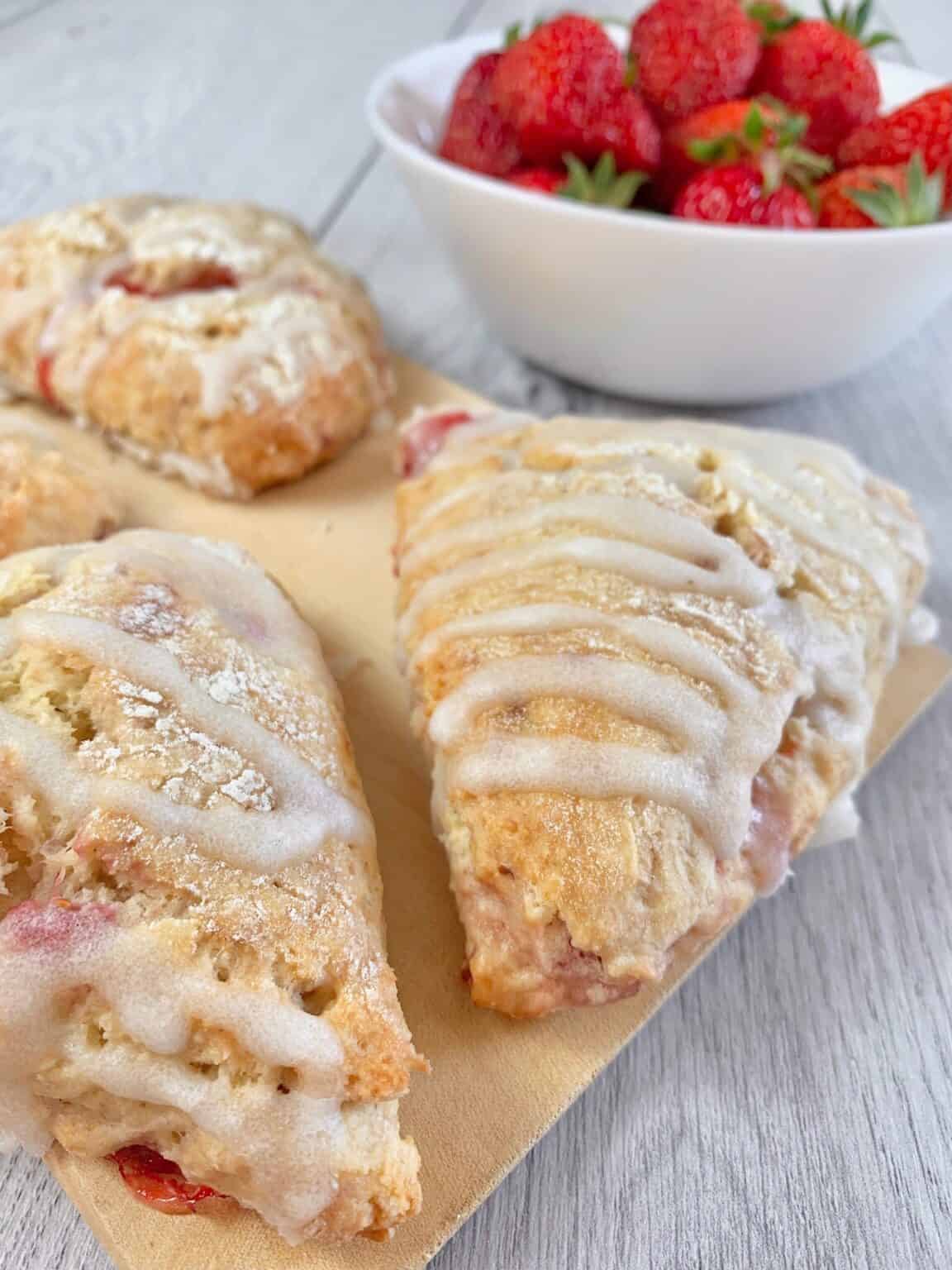 Strawberry scones glazed with vanilla glaze on a wooden board and two fresh strawberries in the front