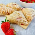 Strawberry scones glazed with vanilla glaze on a wooden board and two fresh strawberries in the front