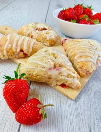 Strawberry scones glazed with vanilla glaze on a wooden board and two fresh strawberries in the front
