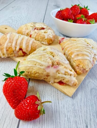 Strawberry scones glazed with vanilla glaze on a wooden board and two fresh strawberries in the front