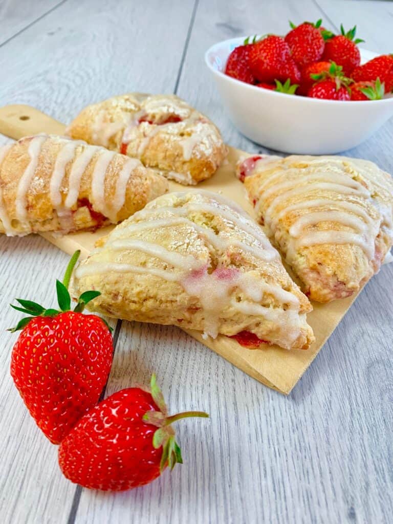 Strawberry scones glazed with vanilla glaze on a wooden board and two fresh strawberries in the front