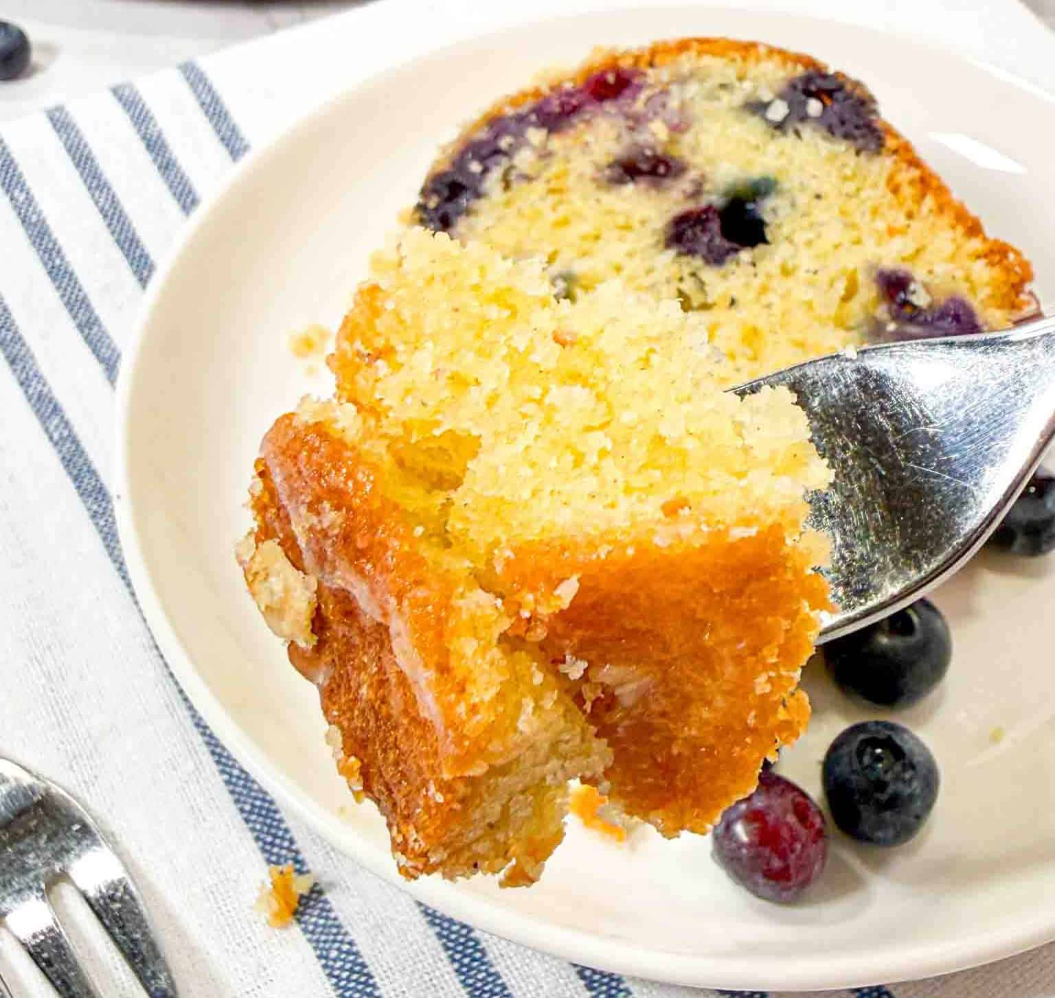 Blueberry Bundt Cake slice on a white plate and a fork picking up a piece