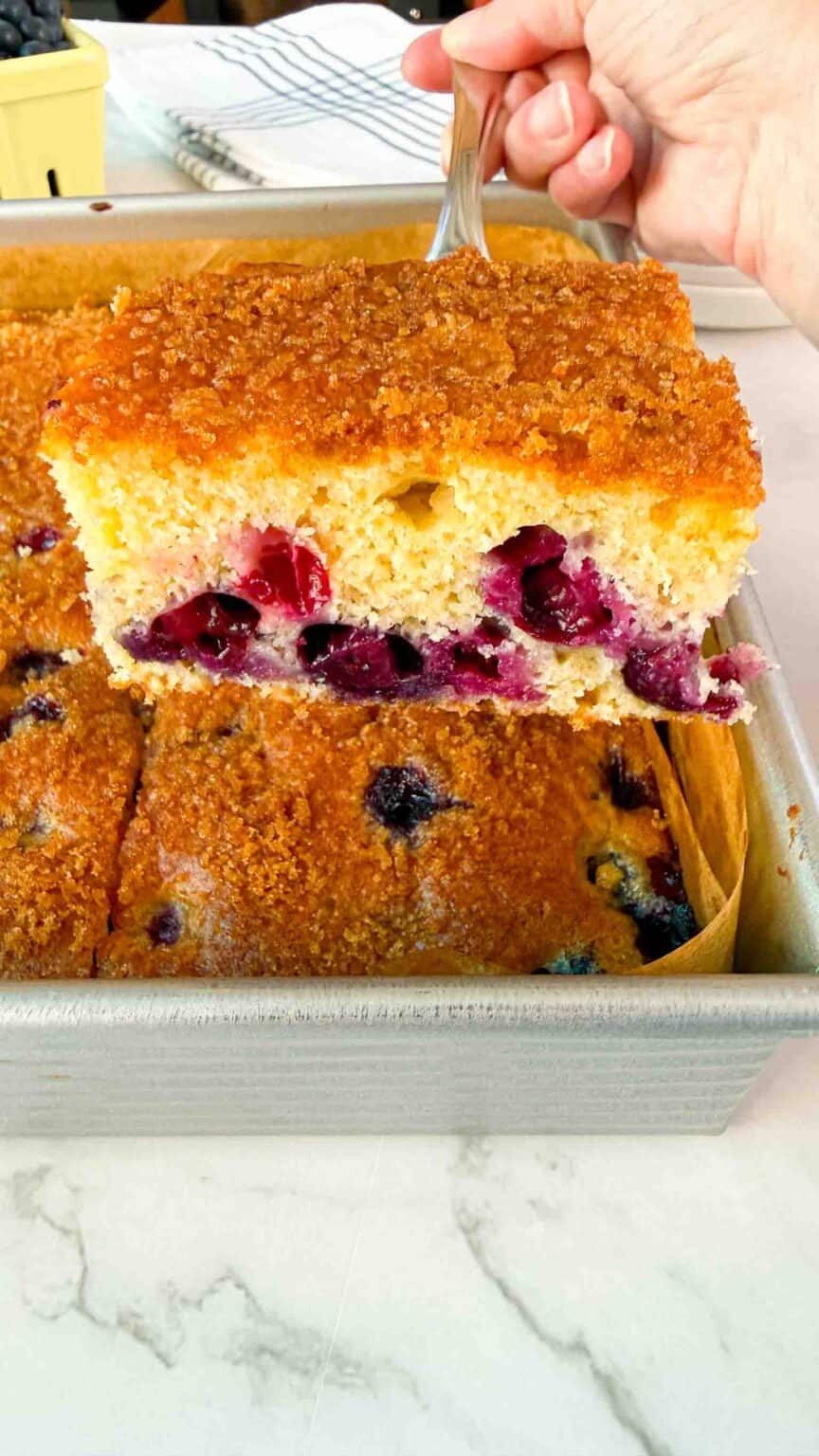 One freshly cut piece of blueberry cake elevated above rest of the cake