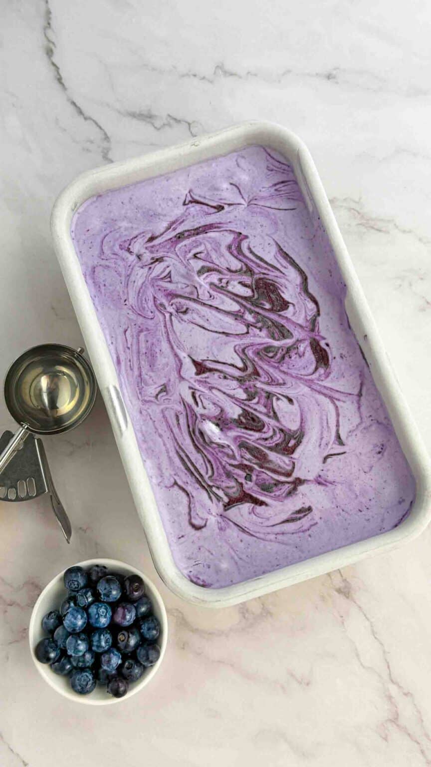 untouched blueberry ice cream in pan with scoop on the side