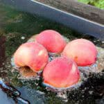 4 half peaches grilling on a griddle with butter and cinnamon