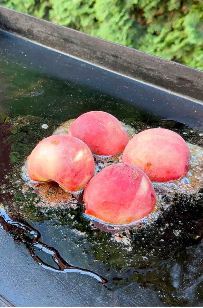 4 half peaches grilling on a griddle with butter and cinnamon