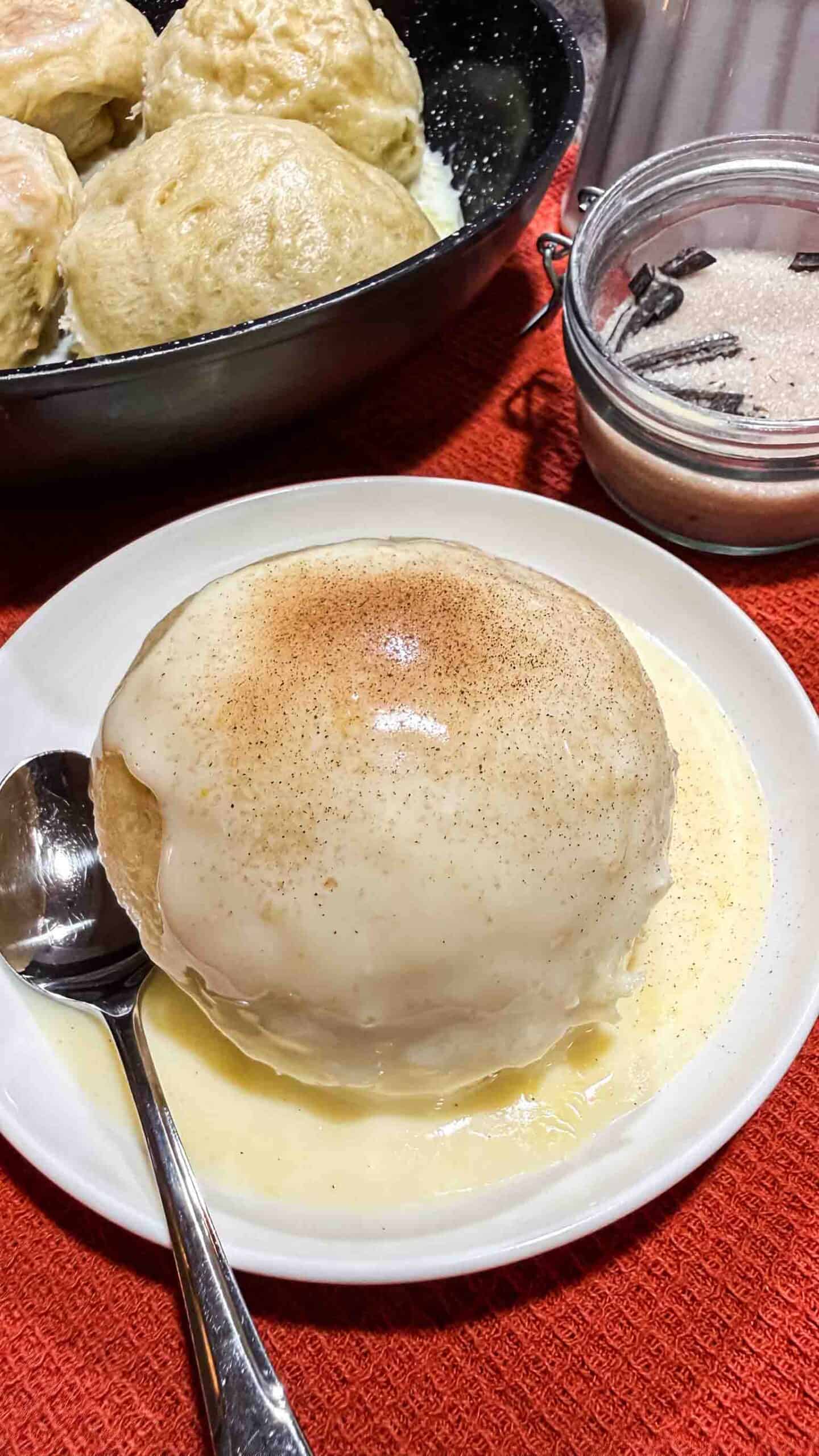 One Dampfnudel topped with vanilla sauce and sprinkled with cinnamon sugar mix