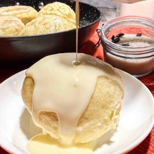 Vanilla sauce drizzeld over warm dampfnudel on a white plate