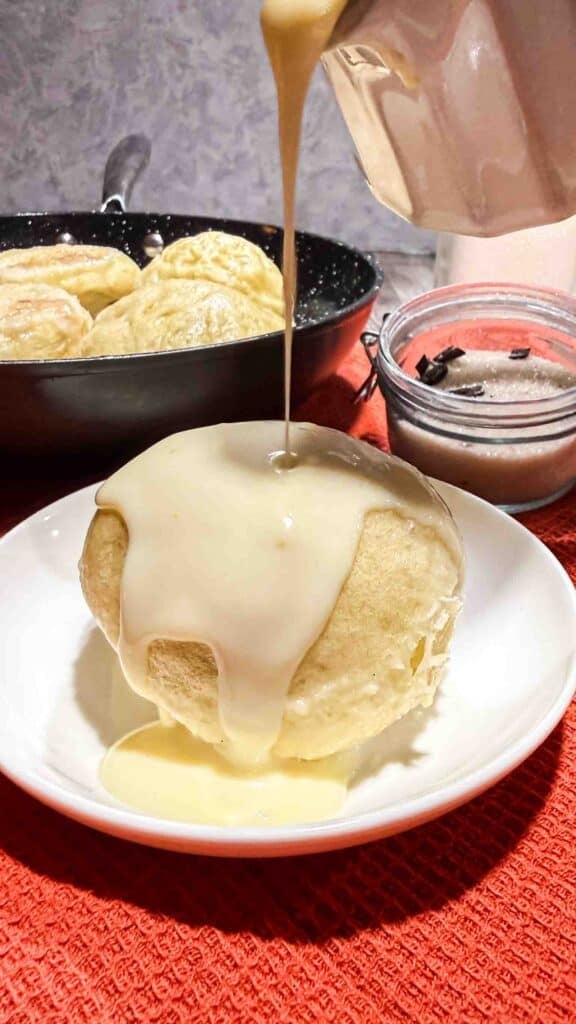 Vanilla sauce drizzeld over warm dampfnudel on a white plate