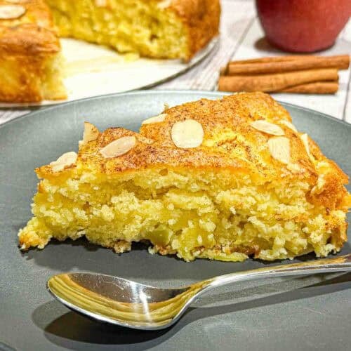 Apple cake slice topped with almond slices on a black plate